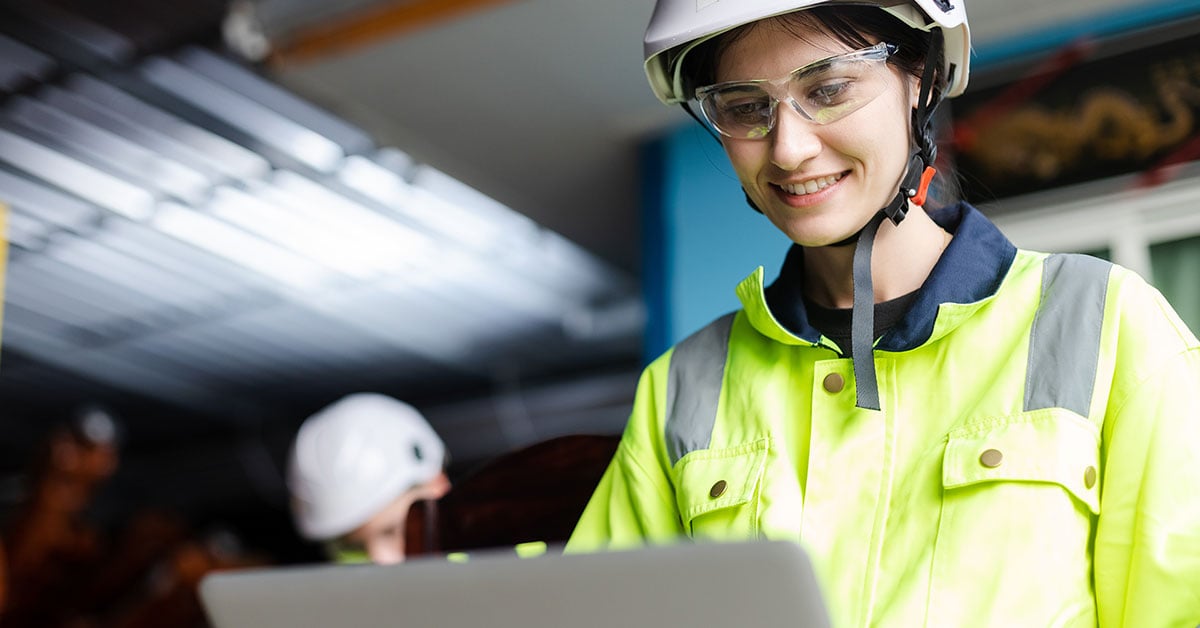 Industrimiljö med varselklädd kvinna med hjälm och bärbar dator